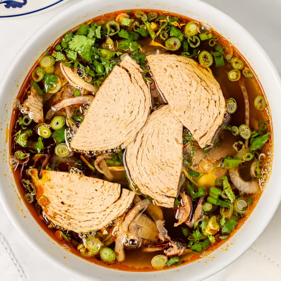 Close-up of a bowl of Bambu Vietnamese Cuisine's spicy beef noodle soup with sliced pork sausage.